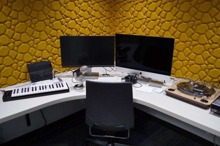 Digital media lab station with monitors and equipment against yellow soundproof wall