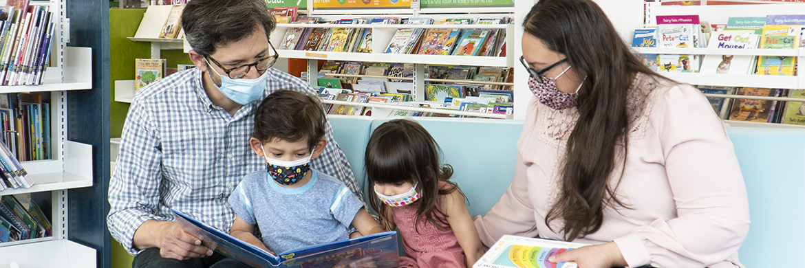 Family sitting an reading in the library with masks on